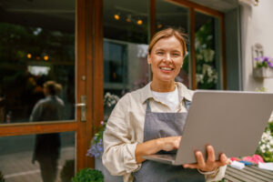 Smiling flower shop owner holding a laptop outside her storefront, representing a small business managing its Google Business Profile category